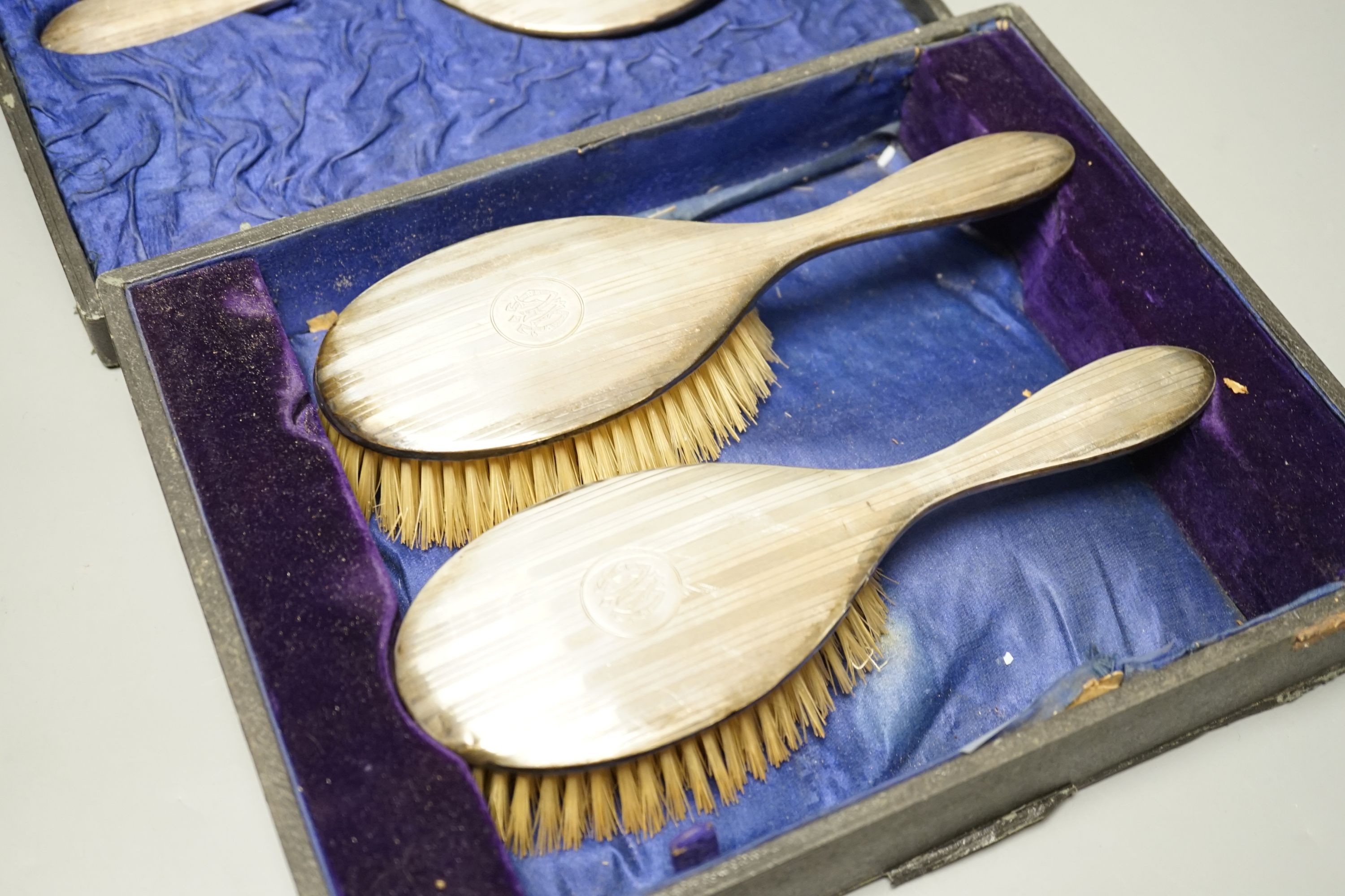 A cased George V three piece silver mounted dressing table set, including a mirror and two brushes.